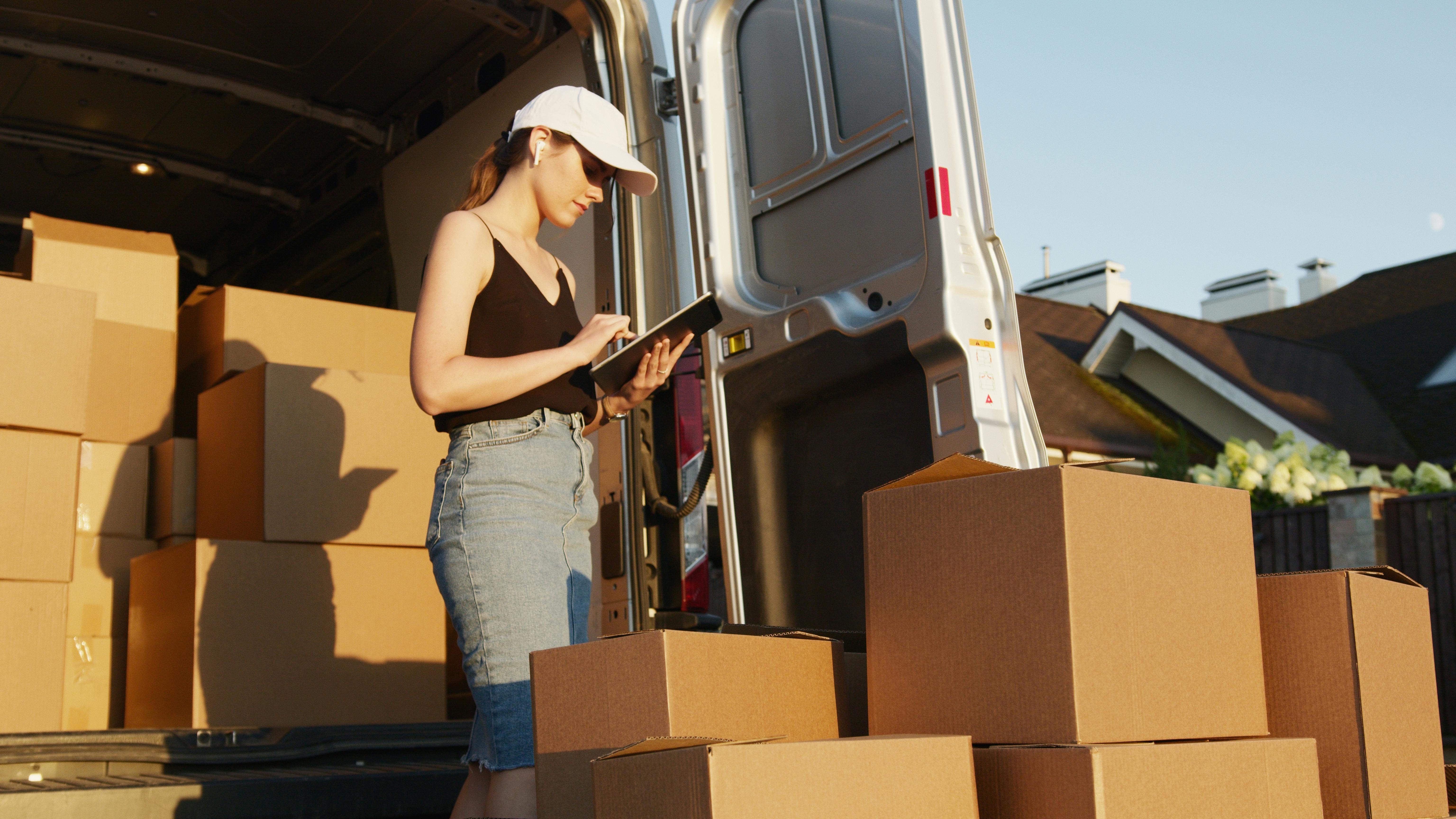 Businesswoman uses a tablet to check inventory as she loads boxes into a truck